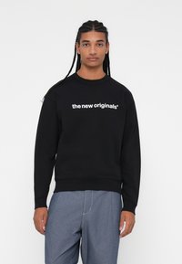 Sweatshirt preto feito de algodão, com decote redondo canelado, apresentando texto branco &quot;os novos originais&quot; na frente e um corte standard.