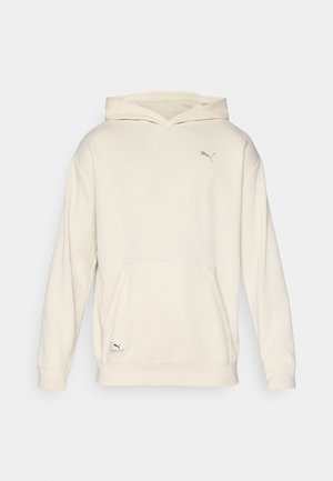 Hoodie beige clair avec un devant texturé, poche kangourou et poignets côtelés. Présente un petit logo en métal argenté sur la poitrine.