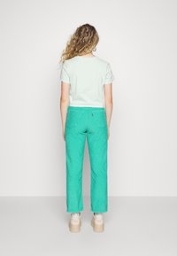 Camisa de manga corta en verde menta combinada con pantalones de pana anchos y texturizados en un azul brillante. Los zapatos tienen una suela gruesa de color claro.