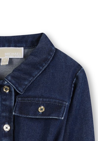 Veste en denim foncé avec un col, des accents dorés sur les boutons et des poches avant. Le tissu a une texture lisse et une coupe classique.