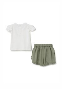 Camiseta de algodón blanca con mangas abullonadas y cierre de botón en la parte posterior, combinada con pantalones cortos de lino verdes con un dobladillo rizado y cintura elástica.