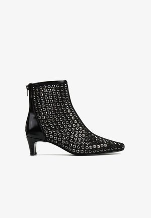 Czarny botek za kostkę z zaostrzonym noskiem, zdobiony metalowymi ćwiekami z przodu, z zamkiem błyskawicznym z tyłu oraz niskim, smukłym obcasem.