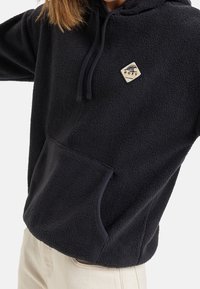 Sweat à capuche en polaire bleu marine foncé, avec une poche frontale, une capuche ajustable et un écusson logo losange crème. Texture douce.