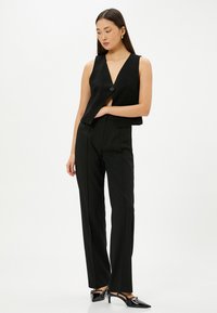 Zwarte op maat gemaakte vest met een diepe V-hals, sluiting met één knop, gecombineerd met rechte broeken. Glad materiaal en gestructureerd ontwerp.