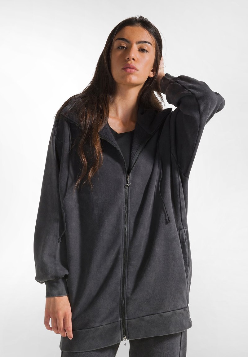 Felpa nera lunga con zip, realizzata in tessuto morbido e dal fit rilassato, con cappuccio regolabile e tasche laterali.