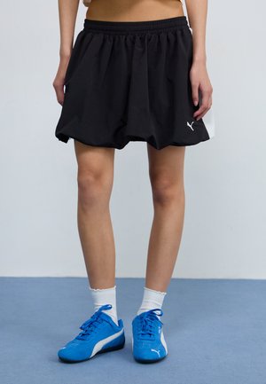 Sorte shorts med elastisk midje, sidelommer, løs passform og hvit logo detalj. Kombinert med blå treningssko og hvite sokker.