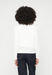 Witte sweatshirt met een ronde hals en ribbelboorden, gecombineerd met donkere spijkerbroeken. De stof lijkt zacht en glad.