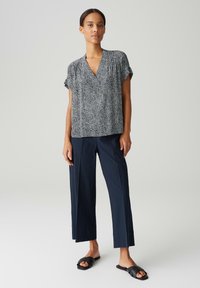 Blusa a maniche corte a righe bianche e nere abbinata a pantaloni larghi blu navy e sandali neri a mocassino. Tessuto liscio, vestibilità comoda.