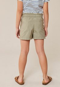Khaakisshorts med elastisk midja, med en enkel design och slät textur, i kombination med bruna sandaler.