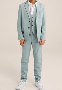 Svetle modrý trojdílný oblek s sakem, vestou a kalhotami, se hnědými knoflíky a bílou košilí, doplněný o bílé tenisky.