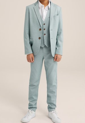 Svetle modrý trojdílný oblek s sakem, vestou a kalhotami, se hnědými knoflíky a bílou košilí, doplněný o bílé tenisky.
