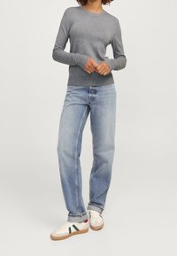 Grå långärmad tröja i ett mjukt tyg, kombinerad med löst sittande blekta blåjeans och vita sneakers med gröna och röda accenter.