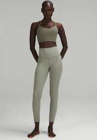 Sujetador deportivo verde oliva con tirantes finos, combinado con leggins de alta cintura de color gris claro, que presentan una tela suave y elástica con costuras que realzan la figura.