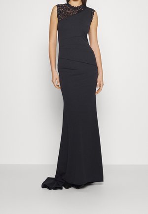 Ärmelloses schwarzes Abendkleid mit Spitzen-Einsatz und tailliertem Oberteil, bodenlanger Rock mit leichtem Schleppe, getragen von einer stehenden Person.