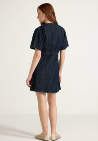 Jeansklänning med korta ärmar, åtsittande midja och utsvängd kjol. Mörkblå färg med synlig sömnad och avslappnad silhuett.