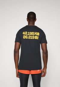 Black cotton t-shirt featuring yellow printed text on the back displaying "42,195 km" and "26.219 mi." Crew neck, short sleeves.