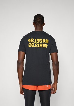 T-shirt en coton noir avec un texte imprimé jaune au dos affichant "42,195 km" et "26,219 mi". Col rond, manches courtes.