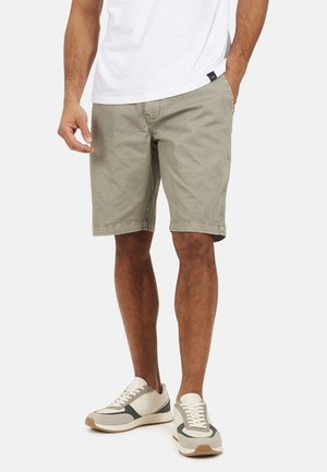 Pantaloni shorts color khaki chiaro con una vestibilità comoda, realizzati in cotone, dotati di tasche laterali e orlo appena sopra il ginocchio, abbinati a sneaker moderne.