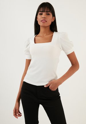 Witte aansluitende top met vierkante halslijn, opgeblazen korte mouwen en gestructureerde stof. Gecombineerd met zwarte broek voor contrast.