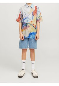 Henkilö, joka on pukeutunut värikkääseen abstraktiin lyhythihaiseen paitaan, vaaleansinisiin farkkushortseihin, valkoisiin nilkkasukkiin, joissa on mustaa tekstiä, ja valkoisiin tenkkuihin.