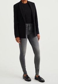 Blazer negro sobre una camiseta negra ajustada, combinado con jeans ajustados grises y mocasines negros. El blazer tiene un diseño entallado y no tiene cierres visibles.
