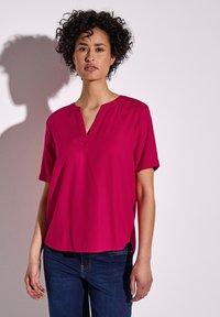 Blusa fucsia a maniche corte con scollatura a V e vestibilità ampia e rilassata. Realizzata in tessuto liscio, presenta sottili spacchi laterali per il comfort.
