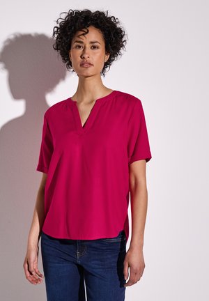 Blouse fuchsia à manches courtes avec un décolleté en V et une coupe décontractée. Fabriquée en tissu lisse, avec des fentes latérales subtiles pour plus de confort.