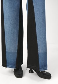 Löyhälahkeiset farkut, joissa on sekoitus sinistä denimiä ja mustia panelia, joiden reunat on purkautuneet. Yhdistetty mustiin korkokenkiin, joissa on neliönmuotoinen varvas.