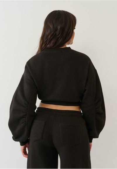 Sweatshirt noir court avec des manches bouffantes, un ourlet côtelé et une texture douce. Assorti à un pantalon de survêtement noir avec des poches arrière.