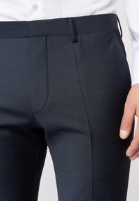 Navy-taillierte Hose aus einem glatten, strukturierten Stoff. Mit flachem Vorderteil, Reißverschluss und dezenten Steppnähten entlang der Taschen.