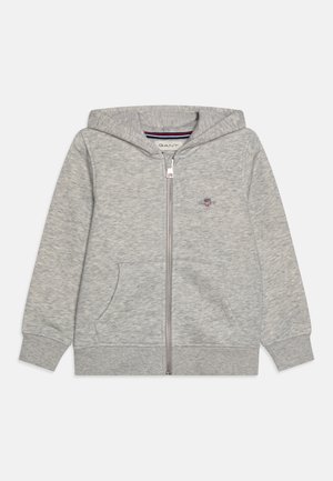 Sivi zip-up dukserica izrađena od mekanog materijala, sa prednjim džepom, rebrastim manžetama i kapuljačom sa prugastom unutrašnjom oblogom. Izvezeni logo na grudima.