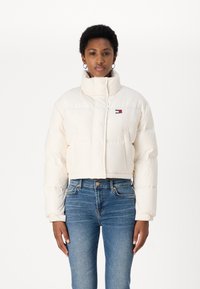 Giacca puffer cropped in bianco sporco, con colletto alto, design trapuntato e piccolo logo multicolore sul lato sinistro del petto.