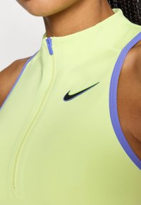 Ανοιχτό πράσινο αμάνικο τοπ με φερμουάρ κλείσιμο, διακοσμημένο με μοβ άκρες. Διαθέτει μαύρο λογότυπο Nike στο μπροστινό μέρος. Ομαλή υφή υφάσματος.
