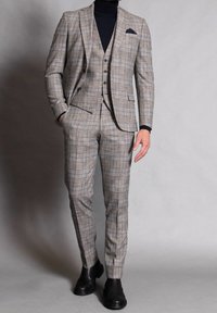 Completo checkered in beige con accenti blu e neri, caratterizzato da un blazer aderente, tre bottoni e pantaloni slim. Stivaletti neri alla caviglia completano il look.