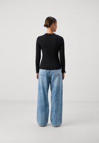 Long-sleeve black top with a textured lace collar, paired with loose-fitting light blue denim jeans with a subtle wash and back pockets.
