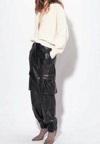 Béžový pletený kardigan s hlubokým výstřihem do V a zapínáním na jeden knoflík, kombinovaný s černými koženými cargo kalhotami s bočními kapsami a elastickými manžetami.