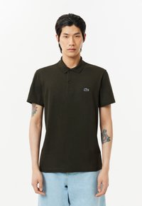 Mörkgrön polo skjorta, bomullstyg, korta ärmar, klassisk krage, tre-knapps knäppning och en liten broderad krokodil-logga på bröstet.