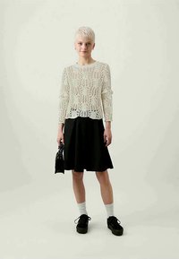Lace-knit light beige sweater, black flared skirt, black platform shoes, white socks, and a small black handbag. Minimalist, casual look.