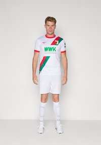 Hvit fotballdrakt med røde detaljer og en diagonalt grønn stripe, med "WWK"-logo. Sammen med hvite shorts og hvite sokker med polstring.