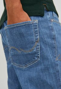 Jeans in denim blu con una finitura testurizzata, dotati di una tasca posteriore con dettagli di cucitura gialla e una vestibilità leggermente ampia.