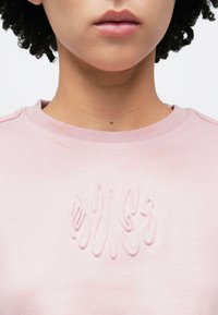 Rózsaszín pulóver puha textúrával, dombornyomott mintával a mellrészen. Bordázott kerek nyakkivágás és laza szabás.