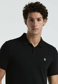 Zwarte polo met een gladde stof, voorzien van een klassieke kraag, drie knopen en een klein wit logo op de linkerkant van de borst.