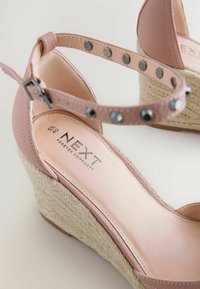 Wedge sandal with pink faux leather upper, textured espadrille platform, adjustable ankle strap with decorative metal studs, logo embossed insole.