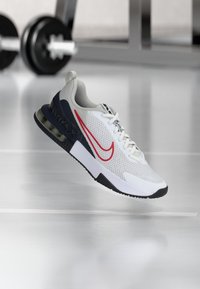 White athletic shoe with red and navy accents. Mesh upper, padded collar, visible Air Max unit, textured sole for grip.