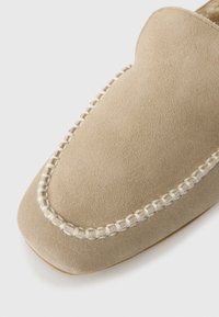 Loafer de camurça bege claro com detalhes brancos visíveis de costura manual ao longo da borda do bico quadrado arredondado.