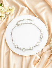 Silverhalsband med runda klara stenar, som växlar med små silverpärlor. Har en kedjeexpander och en hummerklämma. Stylad på en rund vit tallrik.