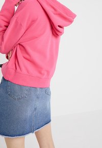 Sudadera rosa hecha de un tejido suave con un bolsillo canguro, combinada con una mini falda de mezclilla azul claro que presenta un dobladillo deshilachado y bolsillos traseros.