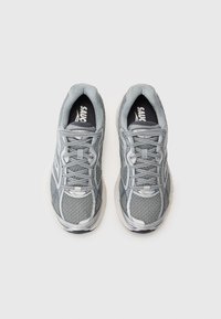 Graue Sportschuhe mit einem Obermaterial aus Mesh, strukturierten Details und gepolsterter Zunge. Sie verfügen über kontrastierende schwarze Einlegesohlen mit "Saucony"-Markenlogo.