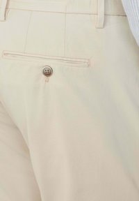 Helle beige Hose mit einer Gesäßtasche, die einen braunen Knopf hat. Der Stoff hat eine glatte Textur und ein flaches Vorderdesign.