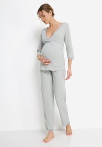 Světle šedé těhotenské pyžamo z měkké látky, obsahující top s výstřihem do V ozdobený krajkou a odpovídající kalhoty s krajkovými lemy.